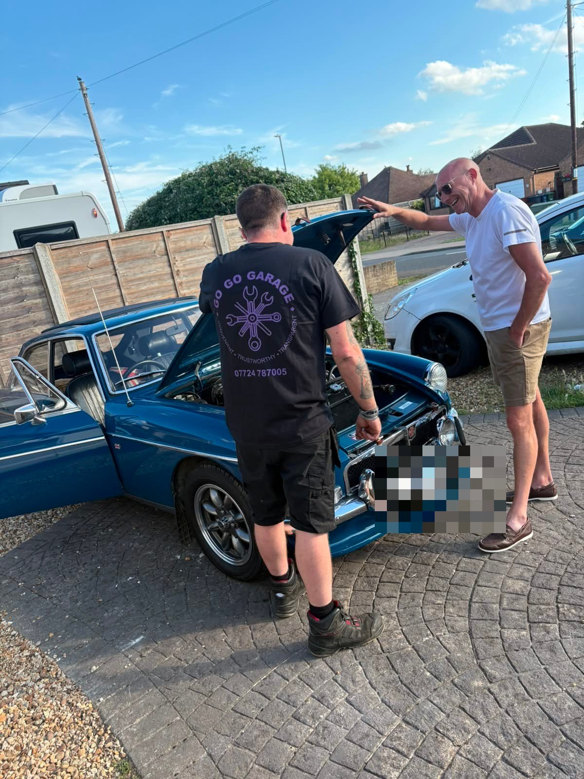 Go Go Garage technician inspecting the engine of a classic blue MGB GT with the owner, Huntingdon, Cambridgeshire